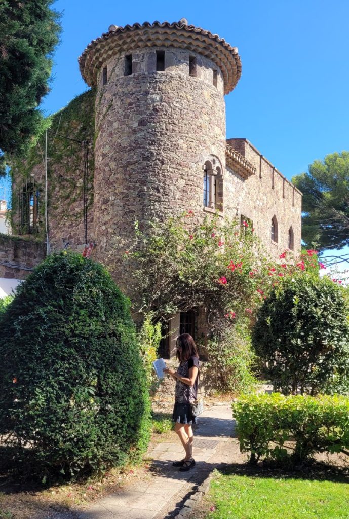 Torre in pietra e giardini del Château de la Napoule, con una visitatrice lungo il vialetto