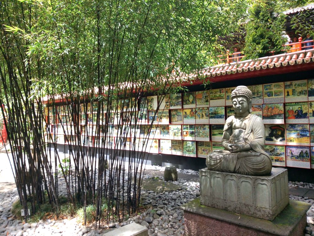 Statua di Buddha nel giardino tropicale Monte Palace a Funchal, Madeira, circondata da bambù e pietre, con pannelli di azulejos dedicati alle avventure dei portoghesi in Giappone