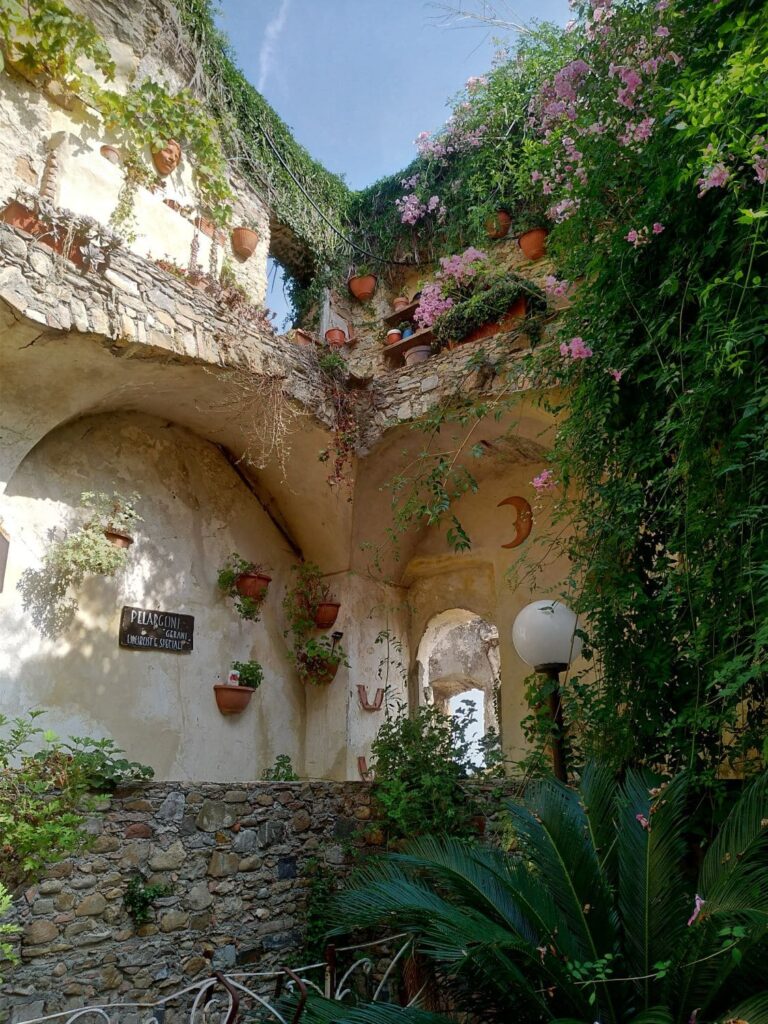 Case in rovina ricoperte dalla vegetazione con opere d'arte e vasi di fiori a Bussana Vecchia.
