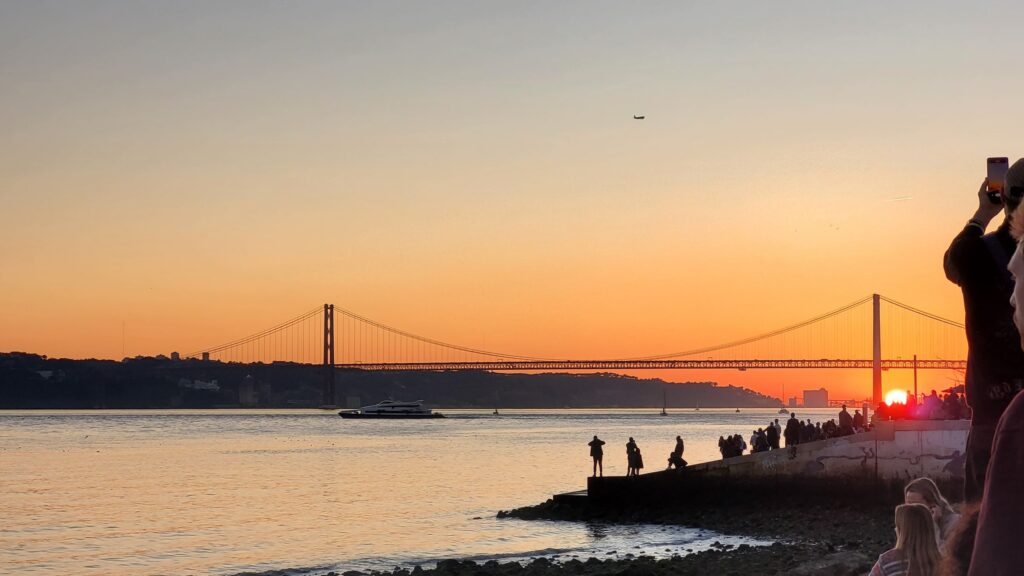 Tramonto sul fiume Tago a Lisbona con il Ponte 25 de Abril sullo sfondo, atmosfera contemplativa di viaggio